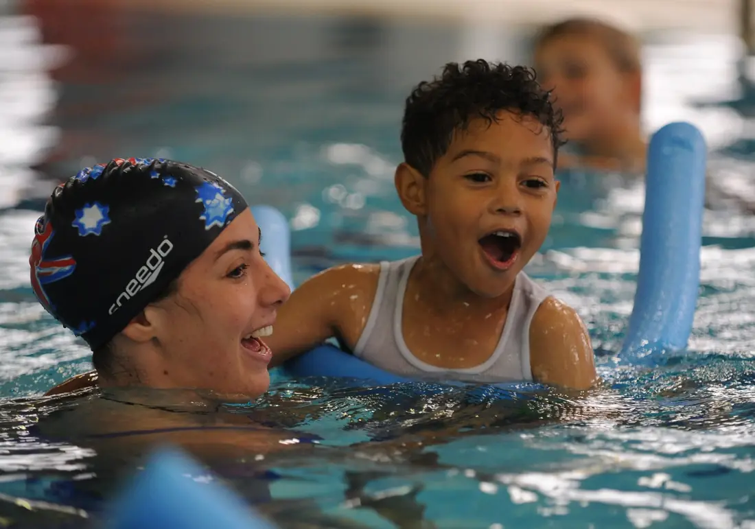 Swim instructor and a delighted young boy holding a pool noodle during a lesson
