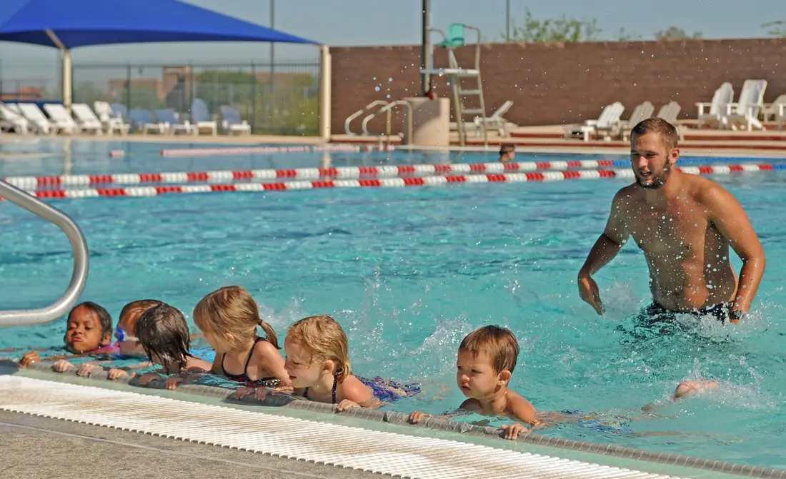Swim instructor in the water coaching a row of young children holding the pool wall